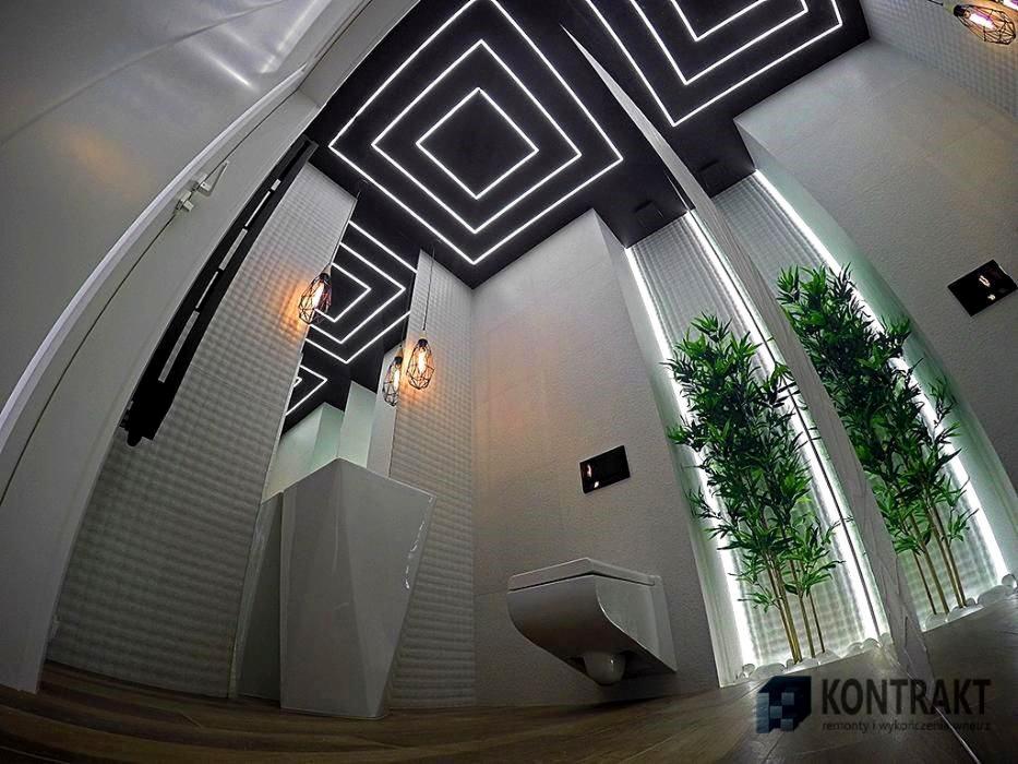 Nowoczesna łazienka z podwieszaną toaletą, umywalką na postumencie i dekoracyjnym oświetleniem sufitowym w geometryczne wzory, uzupełniona bambusowymi roślinami.