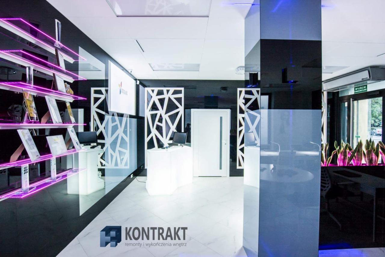 Nowoczesne wnętrze biura z czarno-białą kolorystyką, białymi podświetlanymi meblami, szklanymi półkami z fioletowym oświetleniem i elementami dekoracyjnymi w geometryczne wzory.