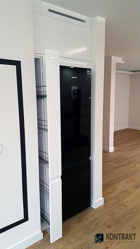 Nowoczesna zabudowa kuchenna z czarną lodówką Samsung i wysuwaną szafką cargo, na tle jasnych ścian i drewnianej podłogi.