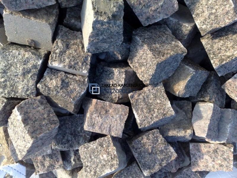 Góra posegregowanych, kolorowych kostek o wymiarach 6x6 cm z granitu o zróżnicowanej fakturze i odcieniach szarości oraz różu, z widocznym znakiem wodnym firmy.