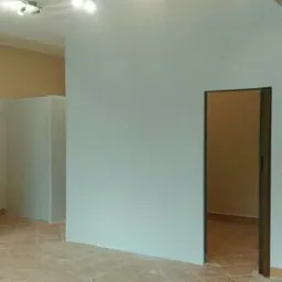 Świeżo pomalowane wnętrze z widocznymi ścianami w odcieniach bieli i beżu, z dwoma otworami drzwiowymi oraz fragmentem czerwonej skrzynki na ścianie.