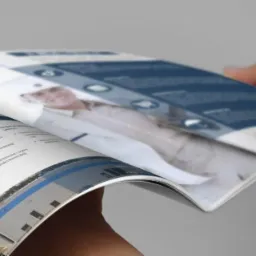 Otwarta broszura firmowa z wizerunkiem inżyniera i budynkiem. Broszura w rękach, prezentuje zakres usług firmy budowlanej w odcieniach bieli i błękitu.