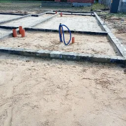 Fundamenty domu jednorodzinnego z widocznymi pionowymi rurami kanalizacyjnymi i niebieskim peszlem instalacji elektrycznej, wypełnione piaskiem.