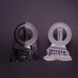 Dwa wydruki 3D w odcieniach szarości przedstawiające model koła z podporami, widoczne ślady warstw druku.