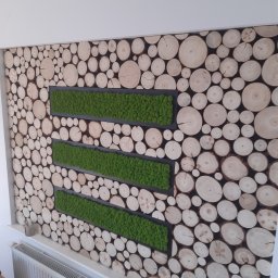 Monter- bud - Ściana z dekoracją z drewna i mchu w trzech poziomych pasach, widoczny grzejnik pod spodem.