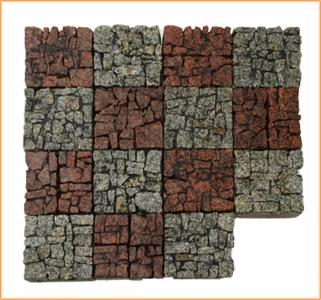 Szachownica z kostki granitowej w odcieniach szarości i czerwieni, ułożona na białym tle. Nietypowy wzór, widoczny brakujący element w prawym dolnym rogu.