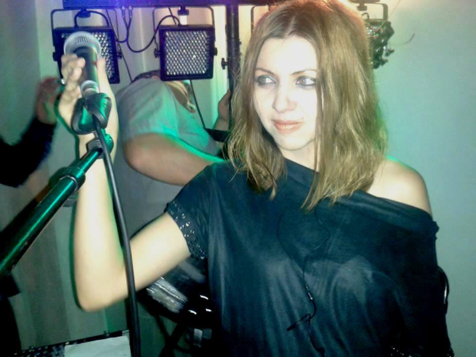 Wokalistka Ewa trzyma mikrofon na scenie z oświetleniem scenicznym w tle.