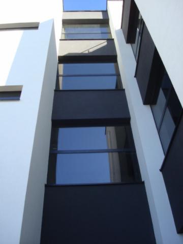 Nowoczesna fasada budynku z oknami, widok z dołu. Białe i grafitowe elementy, minimalistyczny design, błękitne niebo odbite w szybach.