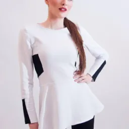 Kobieta prezentuje białą bluzkę z czarnymi wstawkami, stójka, długi rękaw, rozkloszowany dół. Całość na jasnym tle, modelka z kucykiem i makijażem.