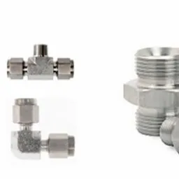 Zestaw złączek metalowych: trójniki i kolanka z gwintem, wykonane z jasnego stopu. Precyzyjne wykonanie, widoczne detale gwintów i połączeń. Białe tło.