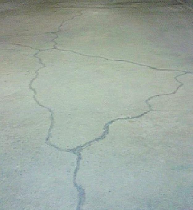 Popękana betonowa posadzka w Przygodzicach, widoczne zarysowania i pęknięcia wypełnione szarym materiałem.