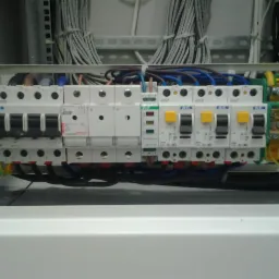 Rozdzielnica elektryczna z zainstalowanymi bezpiecznikami i okablowaniem w skrzynce, widoczne przewody i elementy zabezpieczające.