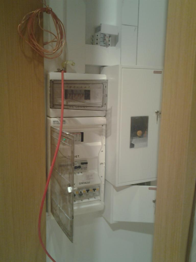 Rozdzielnia elektryczna z otwartymi drzwiczkami, widoczne zabezpieczenia. Instalacja w mieszkaniu w Łodzi. Przewody ułożone w pętlę, gotowe do podłączenia.