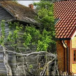 Dom przed i po remoncie w Giżycku: Stara drewniana chata obok nowoczesnego domu z bali z czerwoną dachówką. Kontrast tekstur i kolorów, od zaniedbania do odnowy.