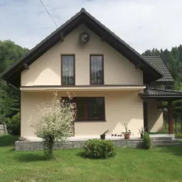 Elewacja domu jednorodzinnego w jasnym odcieniu z ciemnym dachem i oknami, otoczona zielenią. Widoczny satelita na szczycie dachu. Ujęcie z poziomu trawnika.