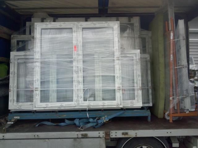 Okna PCV zabezpieczone folią stretch, przewożone na palecie wewnątrz przestrzeni ładunkowej pojazdu dostawczego z niebieskimi pasami mocującymi.