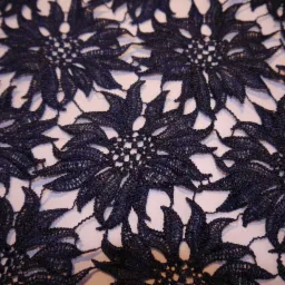 Ciemnoniebieska, koronkowa tkanina z motywem kwiatowym, widoczna z bliska, z delikatnymi prześwitami na białym tle.