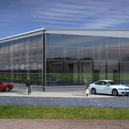 Wizualizacja hali z przeszkloną fasadą, widoczne dwa samochody i przechodzący ludzie. Budynek o szarej elewacji z żółtymi akcentami. Błękitne niebo w tle.