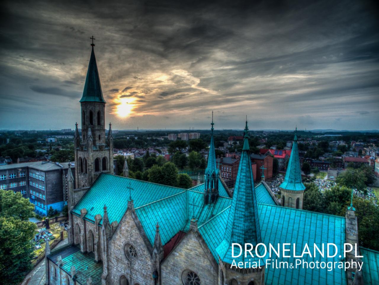 Panorama Chorzowa z lotu ptaka, widok na kościół z turkusowym dachem i wieżą, w tle zachmurzone niebo.
