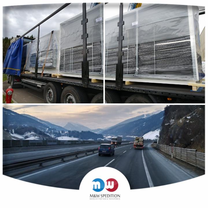 Ciężarówka z niebieską plandeką przewozi ładunek zabezpieczony folią na paletach; w tle widok na górską autostradę i logo firmy spedycyjnej.