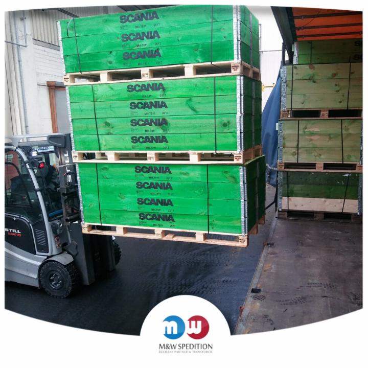 Wózek widłowy STILL podnosi palety z zielonymi skrzyniami oznaczonymi napisem SCANIA podczas załadunku do naczepy ciężarówki.