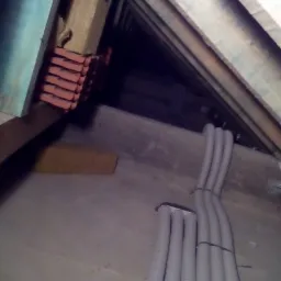 Wiązka szarych, karbowanych rur instalacyjnych, spiętych czarnym zaciskiem, ułożona na szarej powierzchni w surowym wnętrzu z widocznymi elementami konstrukcji drewnianej i stertą pomarańczowych...