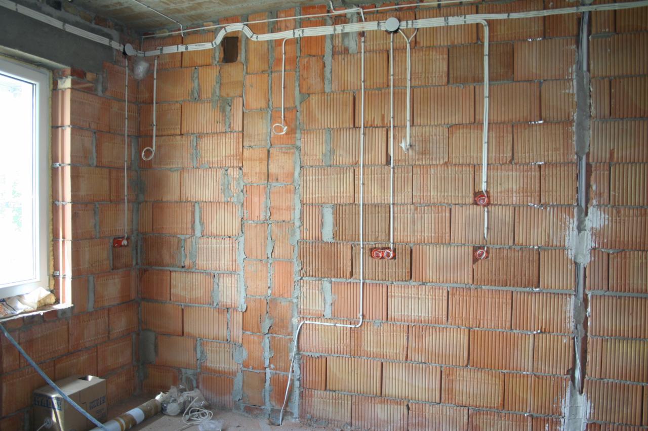Wewnętrzna instalacja elektryczna w surowym budynku: kable prowadzone po ceglanych ścianach, puszki pod gniazdka, okno z lewej strony. Etap prac wykończeniowych.