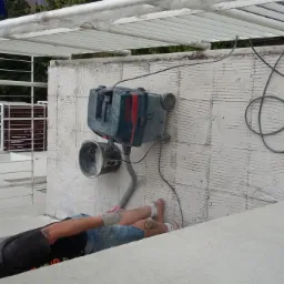 Prace wykończeniowe na balkonie: szlifowanie ściany za pomocą szlifierki z odkurzaczem, przygotowanie podłoża pod malowanie. Widoczna biała konstrukcja balkonu.