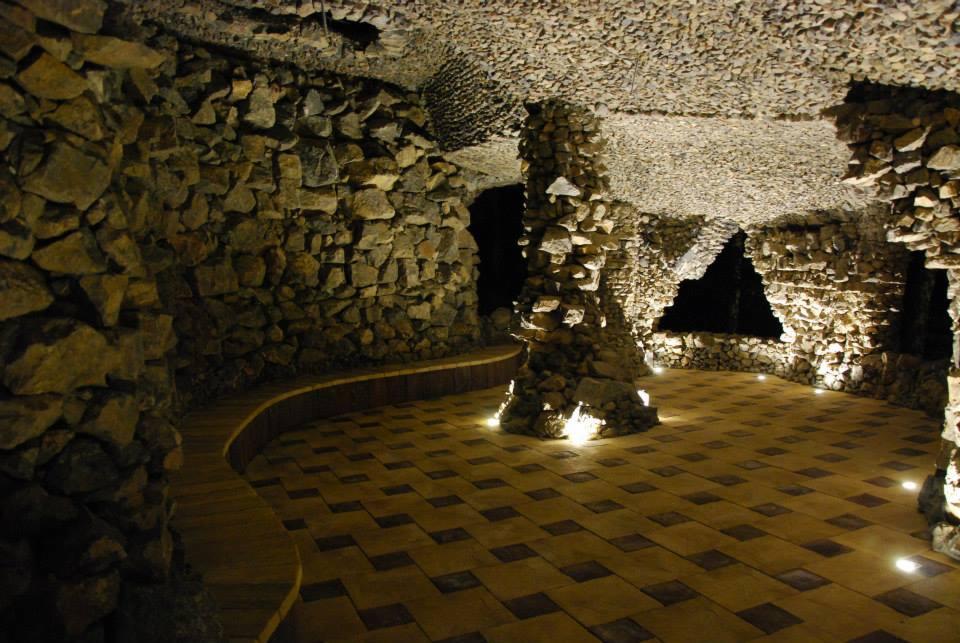 Kamienna grota z podświetlaną podłogą i ławką. Ściany i sufit wyłożone kamieniami, tworzące unikalny, ciemny wystrój wnętrza z punktowym oświetleniem.