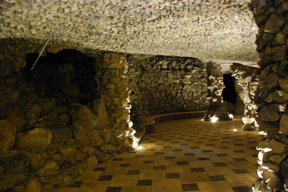 Kamienna grota z podświetlaną ścieżką z płytek i surowym, kamiennym sklepieniem. Nastrojowe oświetlenie punktowe podkreśla fakturę ścian i podłogi.