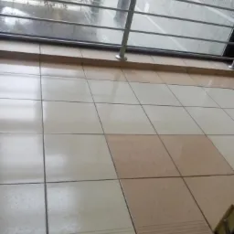 Błyszczące, beżowo-kremowe płytki podłogowe w budynku biurowym, widok przez okno na zewnątrz w deszczowy dzień.