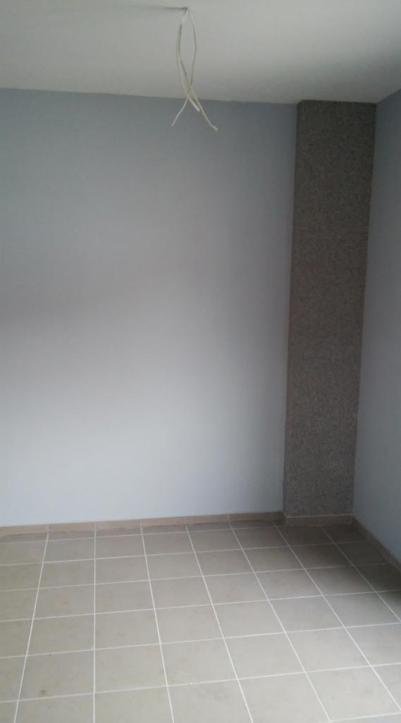 Pomalowane na szaro wnętrze pokoju z wykończonymi płytkami podłogowymi i kolumną dekoracyjną na ścianie; z sufitu zwisają kable.