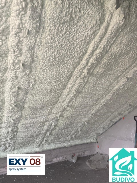 Poddasze po ociepleniu pianką PUR, widoczne nierównomierne nałożenie piany, detale struktury, logo producenta pianki w rogu.