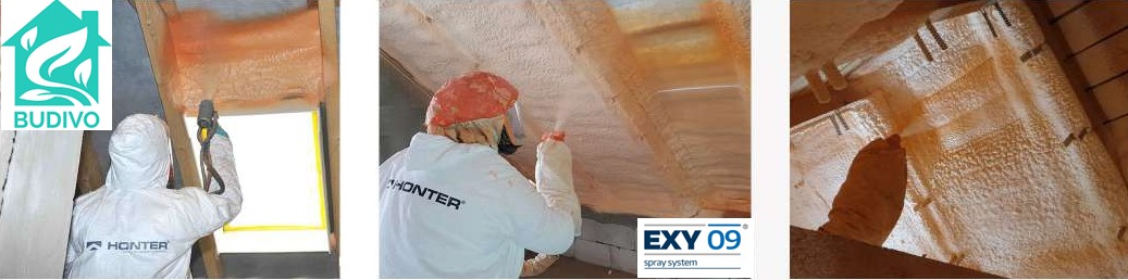 Pracownik w kombinezonie ochronnym aplikuje piankę PUR na poddaszu, widoczne elementy konstrukcji dachu i świeżo nałożona warstwa izolacji. Detal: logo firmy na kombinezonie.