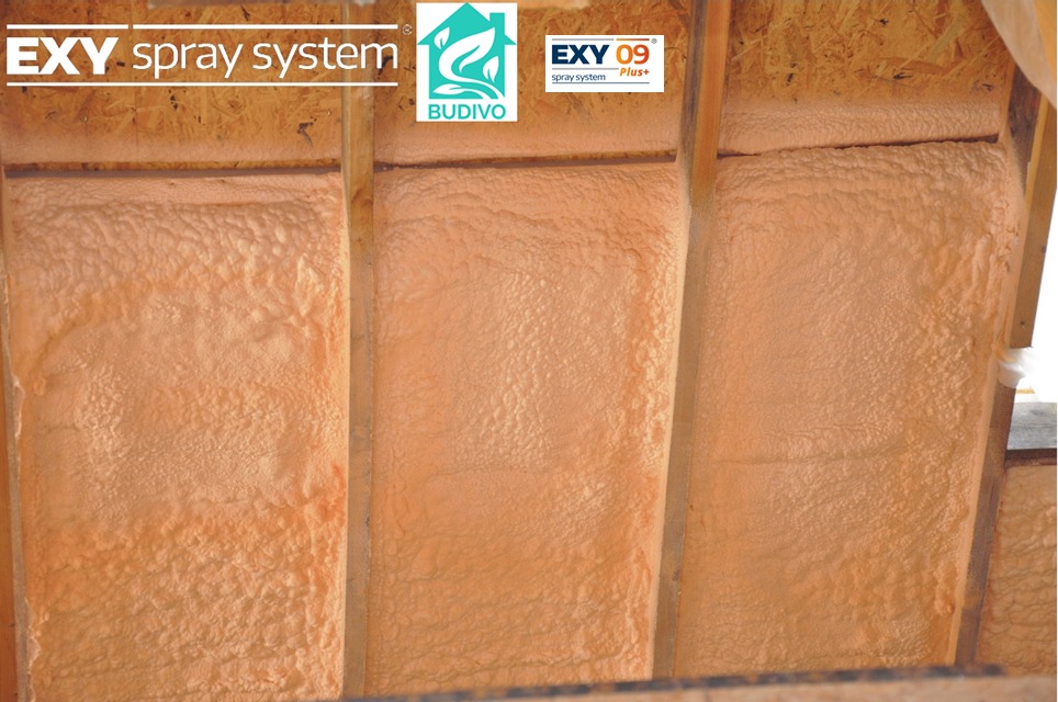 Poddasze ocieplone pianką PUR, widoczne drewniane belki konstrukcyjne i równomiernie nałożona warstwa izolacji w kolorze beżowym. System natryskowy EXY.