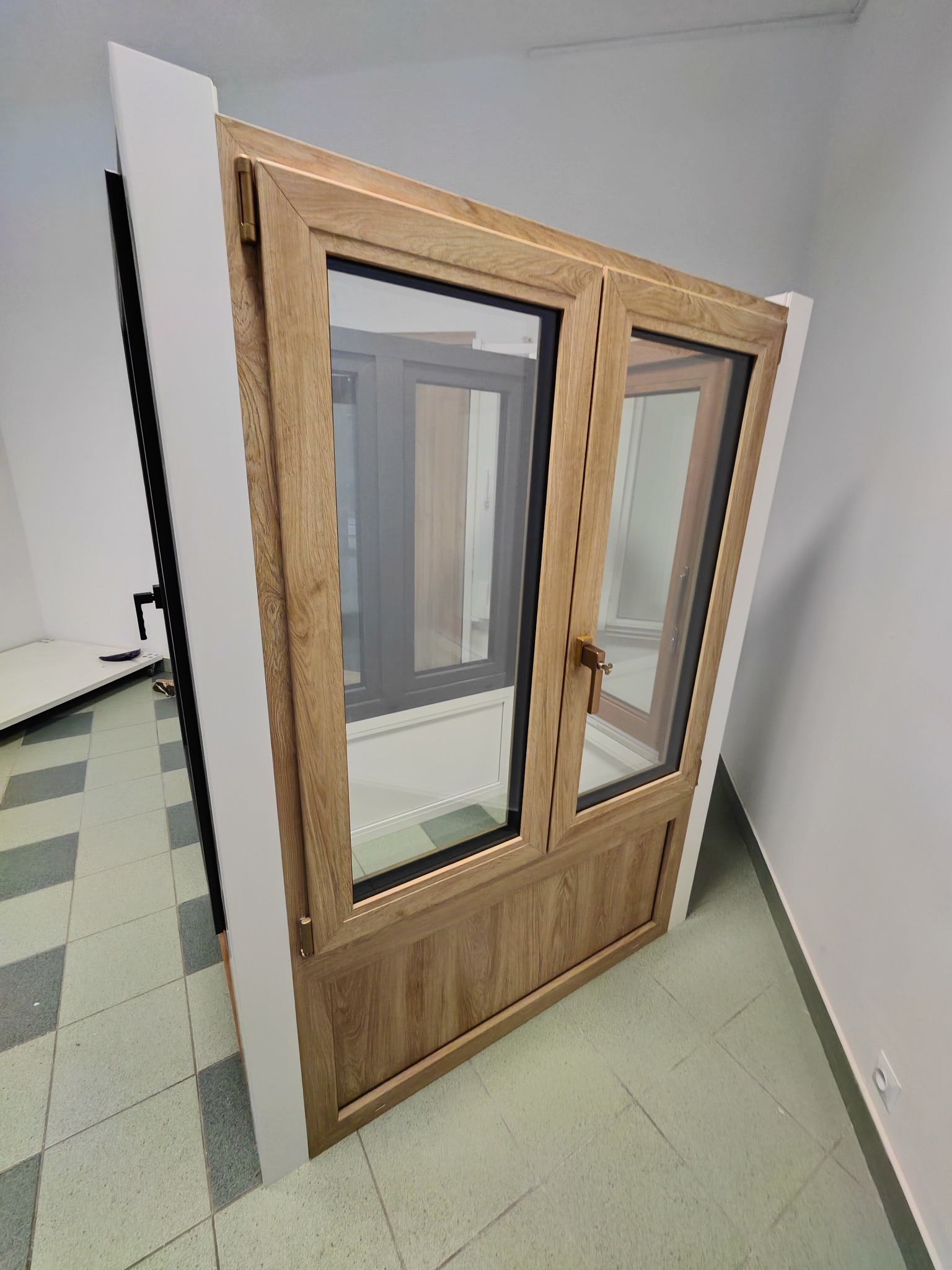 Dwu-skrzydłowe okno z drewnopodobną ramą, widoczne z boku, z uchwytem w kolorze mosiądzu, eksponowane w jasnym pomieszczeniu na tle innych okien.