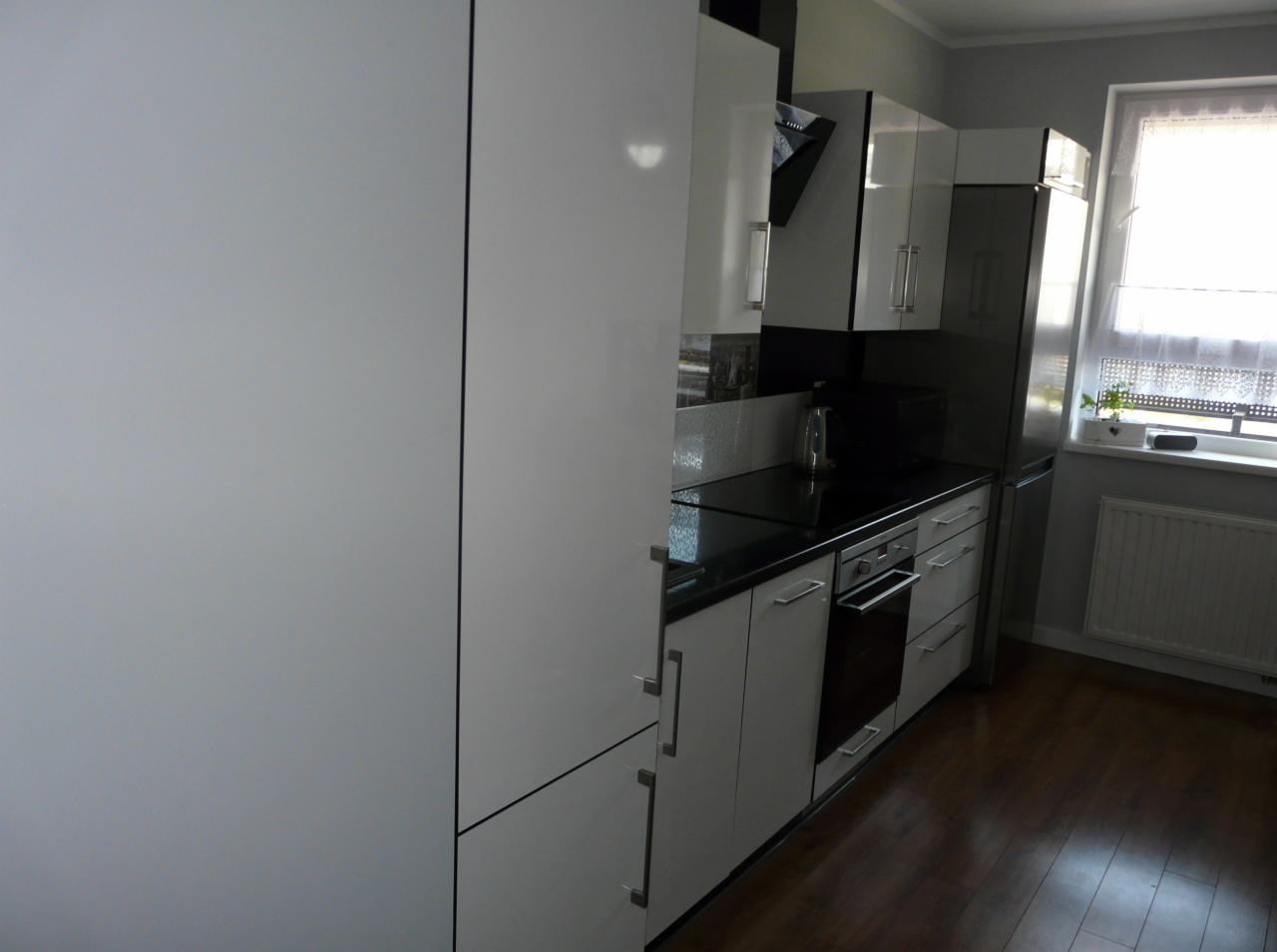 Nowoczesna, biała kuchnia z czarnym blatem i sprzętem AGD, widok z boku na zabudowę kuchenną, drewniana podłoga