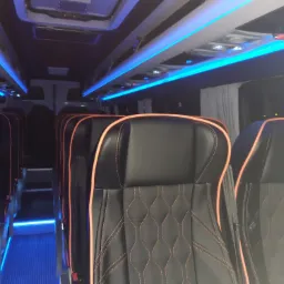 Wnętrze autobusu z czarnymi skórzanymi fotelami obszytymi pomarańczową nicią, oświetlenie sufitowe LED w kolorze niebieskim.