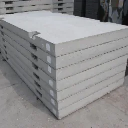 Stos betonowych płyt drogowych z wycięciami na uchwyty, ułożonych na placu budowy. Widoczne etykiety na bokach płyt i faktura betonu.