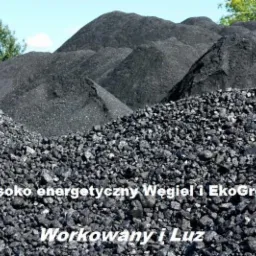 Góry antracytowego węgla na składzie, widoczne bryły o różnej granulacji, z napisem 'Wysoko energetyczny Węgiel i EkoGroszek Workowany i Luz'.