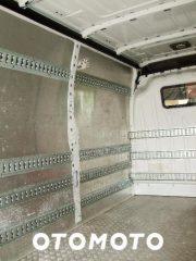 Pusta przestrzeń ładunkowa busa z metalowymi szynami mocującymi na ścianach i podłodze, gotowa do transportu towarów. Widok z wnętrza pojazdu.