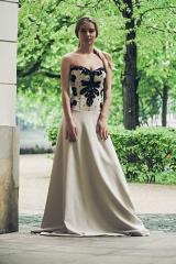 Modelka w długiej, beżowej sukni z czarnym, koronkowym gorsetem pozuje na tle zieleni w plenerze.