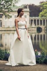 Elegancka kobieta w białej sukni bez ramiączek z czarnym paskiem, pozująca na tle Pałacu na Wodzie w Łazienkach Królewskich.