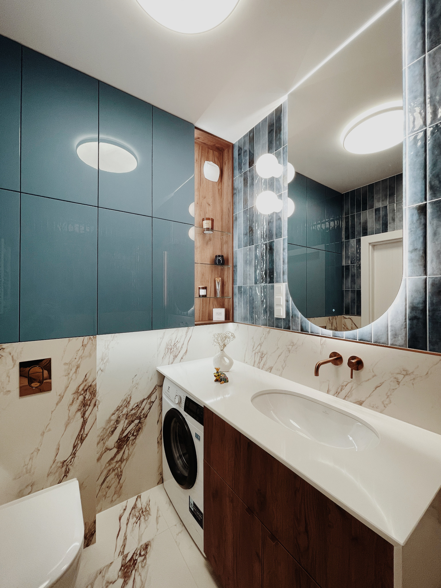 Nowoczesna łazienka w błękitach i bieli: marmurowe ściany, umywalka nablatowa, pralka i szafki z oświetleniem LED. Lustro z podświetleniem.