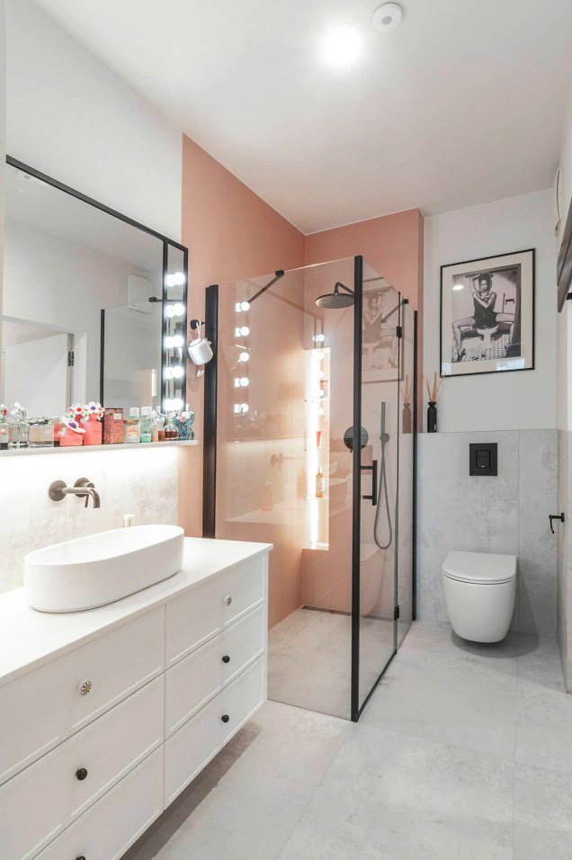 Nowoczesna łazienka z kabiną prysznicową typu walk-in, umywalką nablatową na białej szafce i akcentami w odcieniach różu i czerni.