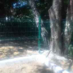 Zielona siatka ogrodzeniowa zamontowana wokół drzewa, widoczny betonowy fundament.