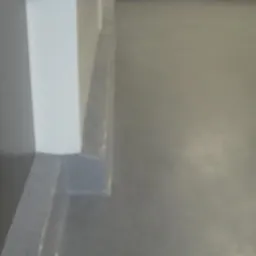 Szara, gładka posadzka w pomieszczeniu, z widocznym fragmentem białej ściany i szarą listwą przypodłogową. Minimalistyczne wykończenie.