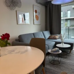 Jasnoszary narożnik w nowoczesnym salonie z wyjściem na balkon, na podłodze szara pleciona struktura.