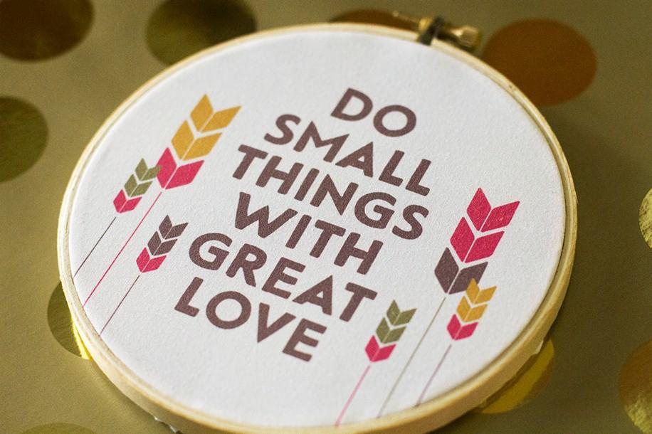 Okrągła rama z napisem 'Do small things with great love' i motywem strzałek w kolorach: żółtym, czerwonym i brązowym na tle w złote kropki.