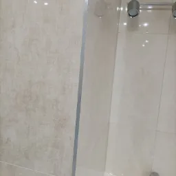 Beżowe, błyszczące płytki w łazience, zamontowane przy wannie, widoczny srebrny reling na ręczniki i bateria umywalkowa.